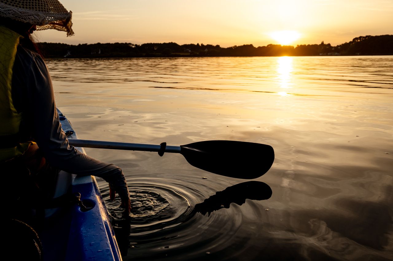 A peaceful kayaking scene captured at sunset with reflections on a calm lake surface.